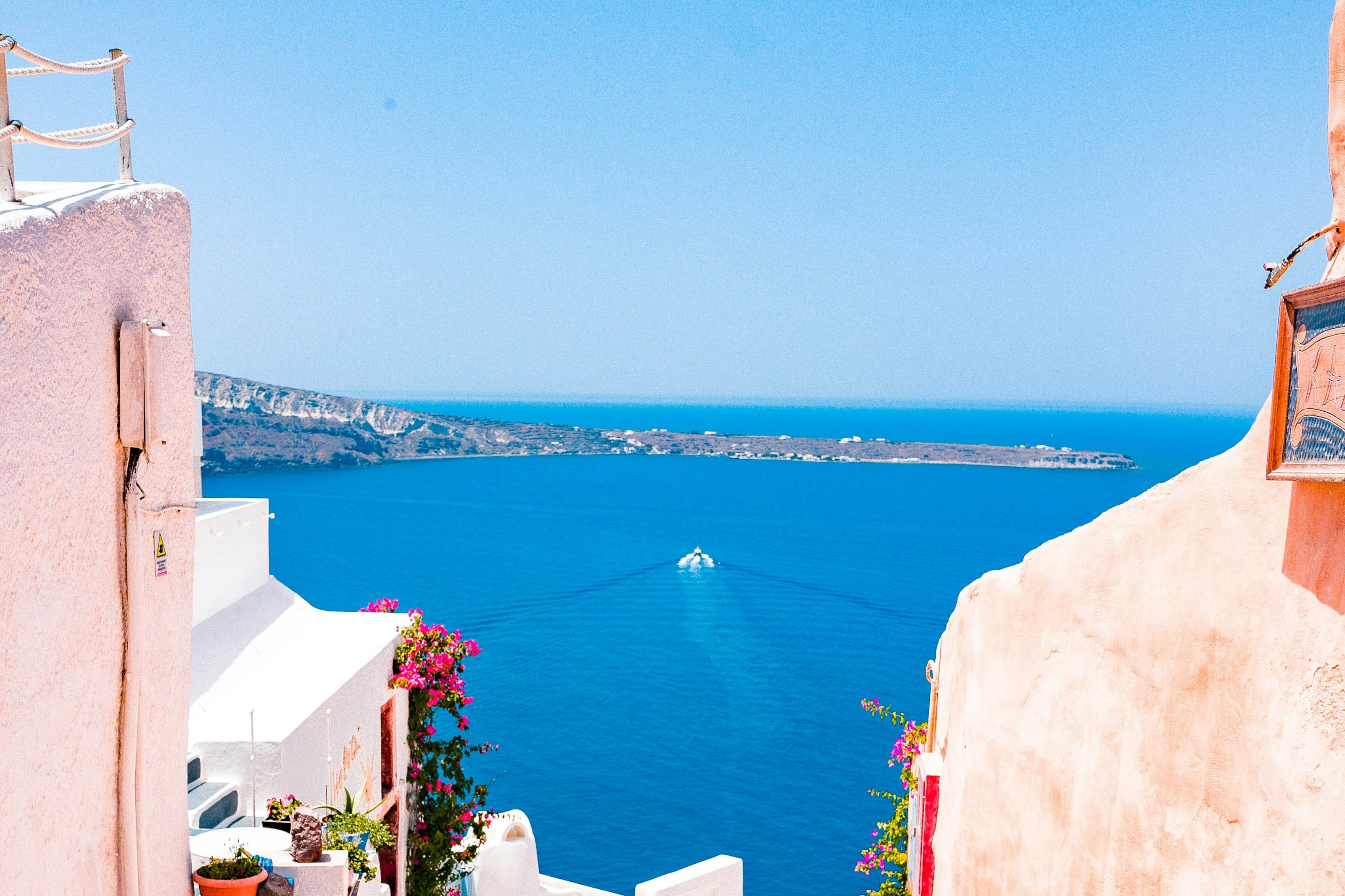 A whitewashed alley opening onto deep blue Aegean water and a distant headland