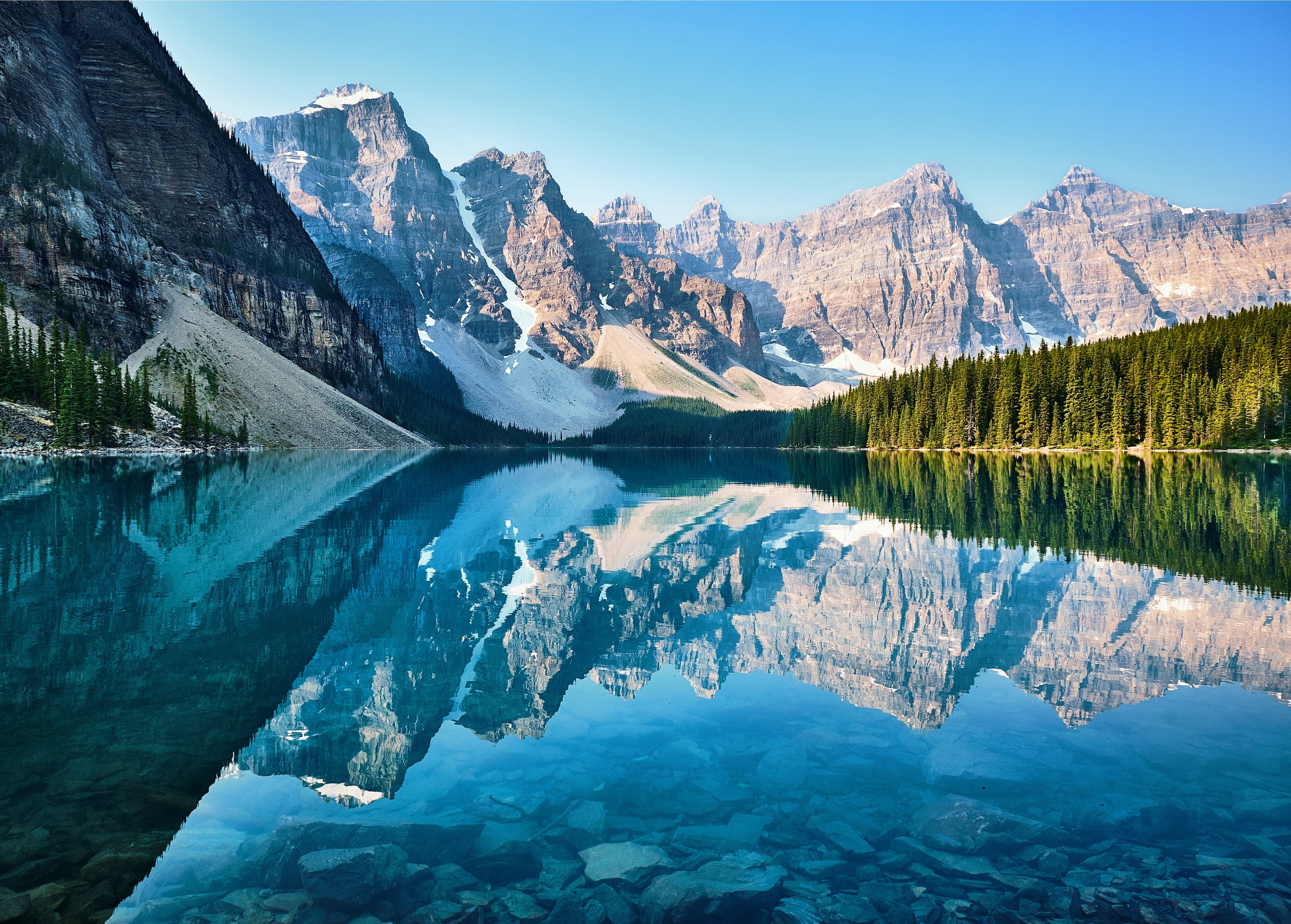 Snow-capped peaks reflected in a still alpine lake ringed by pine forest