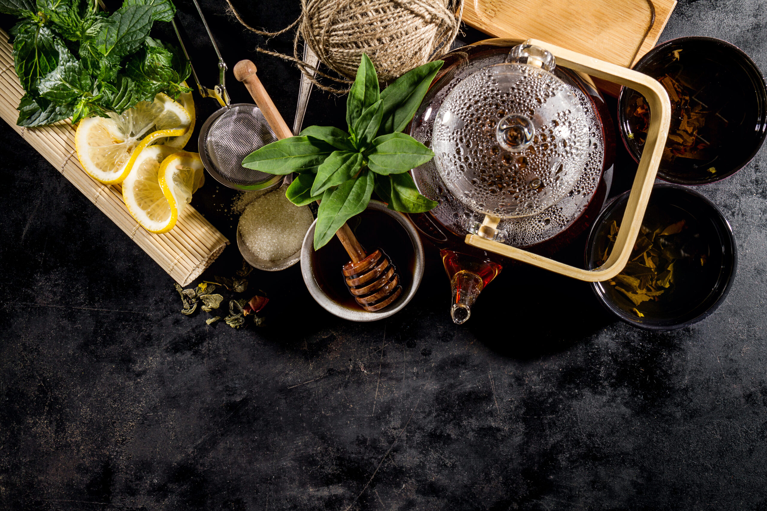 Beautiful Tea Ceremony Glass Teapot Honey Mint Lemon Cups on Dark Table Background Closeup Horizontal